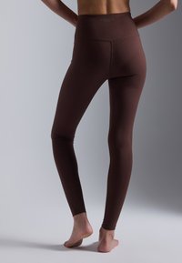 Brown high-waisted leggings in a smooth, stretchy fabric, featuring a seamless design and fitted silhouette, with no visible branding.