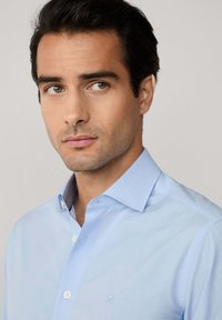 Camisa de vestir azul claro con un corte entallado, cuello button-down y un discreto acento bordado. Tejido suave con cierres de botones.
