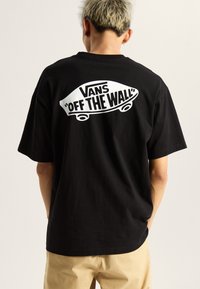 Camiseta de algodón negra con un gran gráfico en blanco del logo "Vans 'OFF THE WALL'" en la parte posterior, mangas cortas y un corte relajado.