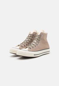 Sneakers înalte dintr-un canvas bej deschis, cu accente bej, șireturi texturate și o talpă din cauciuc albă ce prezintă o dunga neagră.