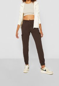 Bruine cargo broeken met elastische manchetten, zijzakken en een knoopsluiting. Gepaard met een beige cropped top en witte sneakers.