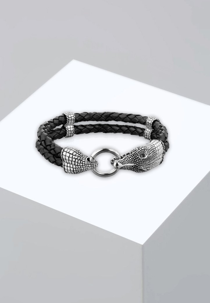 Svart flätad läderarmband med två silverfärgade djurhuvuden som lås, med detaljerade texturer och en cirkulär metallring som förbindelse.