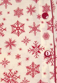 Motivi di fiocchi di neve rossi su tessuto crema, con dettagli a bottone e una texture fine. Il design include diverse forme e dimensioni di fiocchi di neve.