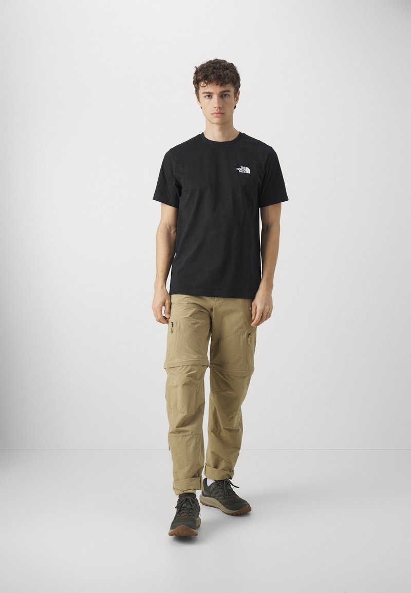 Black short-sleeve t-shirt with white logo on the chest, paired with khaki cargo pants featuring zippered pockets and a loose fit.
