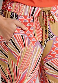 Elastische broek met grote, kleurrijke bladdessins in roze, rood en lavendel, met diagonale strepen en zijzakken.
