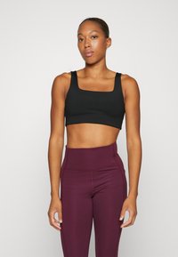 Black sports bra with a square neckline and wide straps. Paired with high-waisted, burgundy leggings. Smooth, stretchy fabric.