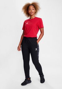 Rød kortærmet t-shirt parret med sorte tapered sweatpants med grå chevron-striber på siden og elastisk talje. Sorte træningssko.