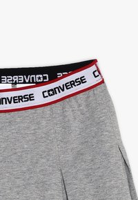 Šedé šortky s širokým elastickým pasem, který má červené a bílé detaily. Na přední straně pásu je černě natištěno "Converse".