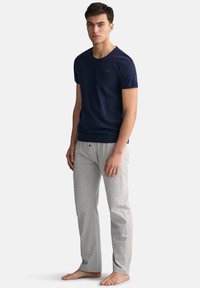 Merihenkinen crew-neck t-paita yhdistettynä vaaleanharmaisiin lounge-housuihin. Kangas näyttää pehmeältä, rento istuvuus ja minimalistinen brändäys paidassa.
