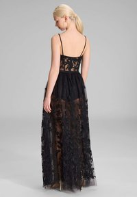 Schwarzes Abendkleid mit durchsichtiger Tüllüberlage und floralem Stickerei, schmalen Trägern und einem taillierten Oberteil. A-Linie Silhouette mit fließendem Rock.
