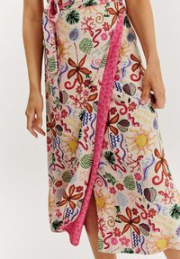 Zavinovací sukně s růžovým pozadím a barevnými květinovými a abstraktními vzory, zdobená bočním rozparkem a zavazováním v pase.