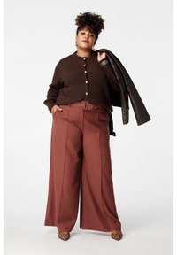 Cardigan marron en maille avec boutons, associé à un pantalon large rouille avec ceinture. Talons à motif animal complètent le look.