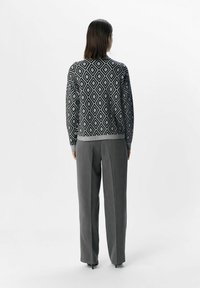 Schwarzer und weißer Pullover mit Diamantmuster, graue Hose, mit gerippten Bündchen und Saum, von hinten vor einem schlichten Hintergrund gezeigt.