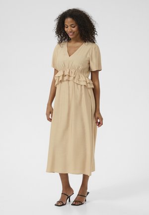 Beige midi-jurk met korte mouwen, volantdetails bij de taille en een V-halslijn. Soepele textuur, gecombineerd met zwarte gesp sandals.