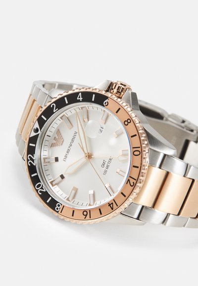 Silber- und goldfarbene Edelstahl-Uhr mit Zifferblatt in Weiß, schwarzem und goldfarbenem Gehäuse sowie markanten Stundenmarkierungen. Verfügt über eine Datumsanzeige und eine GMT-Funktion.