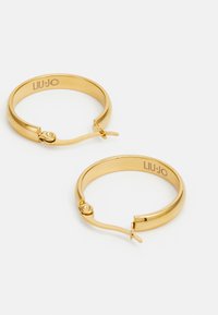 Gold hoop earrings featuring a simple design, smooth texture, and a secure closure mechanism. Engraved branding on the inner surface.