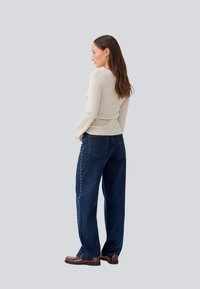 Beige ribbed long-sleeve top paired with dark blue wide-leg jeans featuring a button detail along the side. Worn with brown shoes.