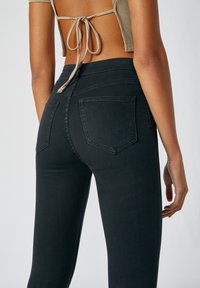 Jeans negros de cintura alta con una textura suave, que cuentan con bolsillos traseros y sutiles detalles de costura. El corte es ajustado y entallado.