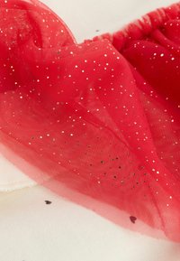 Rød tylstof med guldglitter accenter lagd over en hvid baggrund. Har en blød tekstur og en semi-gennemsigtig fremtoning.