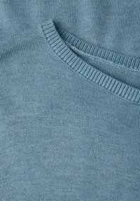 Tessuto lavorato a maglia blu chiaro con scollatura tonda. La texture è liscia e densa, mostrando fibre fine e sottili variazioni di colore.