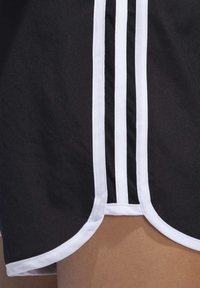 Shorts deportivos negros con ribete blanco, que presentan tres franjas verticales blancas a los lados y un dobladillo curvado en la parte inferior.