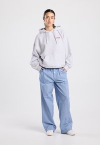 Sweat à capuche gris clair avec une poche avant et des cordons de serrage, associé à un pantalon large rayé bleu et des chaussures blanches.