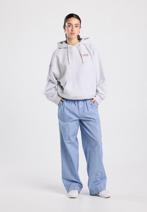 Light gray hoodie featuring a front pocket and drawstrings, paired with blue striped wide-leg pants and white shoes.