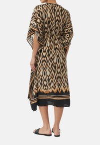 Sukienka w stylu kimono z czarnym, kremowym i brązowym wzorem ikat. Luźny krój, zwiewne rękawy oraz dół ozdobiony wzorzystą lamówką.