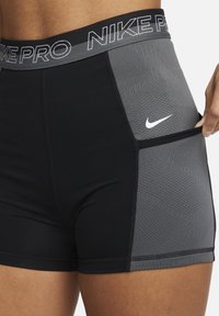 Czarne i szare szorty Nike Pro. Dopasowany krój, teksturowana szara wstawka z sześciokątnym wzorem oraz boczna kieszeń. Odbijające światło logo z przodu.