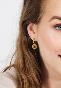 Gouden hoepel oorbellen met een ronde hanger, gekenmerkt door een gladde textuur en een minimalistisch ontwerp, hangend aan een kleine hoepel bevestiging.