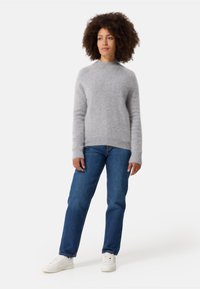 Maglione grigio chiaro e lanoso con collo alto, maniche lunghe e orlo a coste, abbinato a jeans blu classici e sneakers bianche.