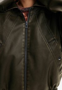 Olive green faux leather jacket with a zip closure, ribbed cuffs, and a hood. Features panel stitching and glossy accents.