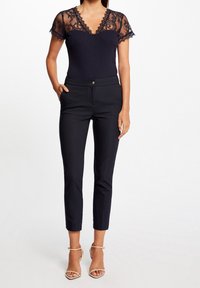 Sort bodysuit med blondermanchetter og V-hals, parret med skræddersyede sorte bukser med knaplukning og cropped længde.