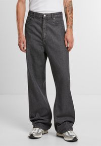Bredde ben mørkegrå denimjeans med frontlommer, en knappelukking og subtile sømdetaljer. Brukt med grå og hvite joggesko.