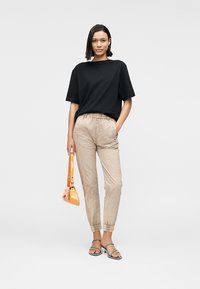 Μαύρο υπερμεγέθες μπλουζάκι, μπεζ παντελόνι με ελαστική μέση και υφασμένο σχέδιο, και πορτοκαλί τσάντα χειρός. Μοντέλο φοράει ασημένια σανδάλια με λουράκια.