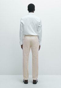 White collared shirt with long sleeves, paired with light beige trousers. The pants feature a smooth texture and back pockets, completed with dark shoes.
