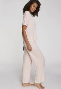 Ensemble de pyjama rose clair côtelé comprenant un haut à manches courtes ample et un pantalon à jambes larges, avec des fentes latérales pour un confort accru.
