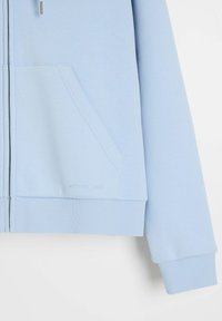 Jasnoniebieska bluza rozpinana na zamek, z elastycznym ściągaczem u dołu i na mankietach, kieszenią kangurką oraz małym wytłoczonym logo "diverse" w pobliżu kieszeni.