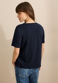 Camiseta azul marino de manga corta con escote de cuello redondo, hecha de una tela suave. Combinada con jeans de mezclilla de color azul claro.