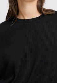 Schwarzes, geripptes langärmliges Oberteil mit Rundhalsausschnitt. Der Stoff hat ein strukturiertes Muster und besteht aus einem weichen, elastischen Material.