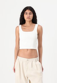 Hvit stripete kuttet tanktopp med firkantet utringning og brede stropper, stylet med beige løstsittende bukser. Ingen synlige logoer eller mønstre.