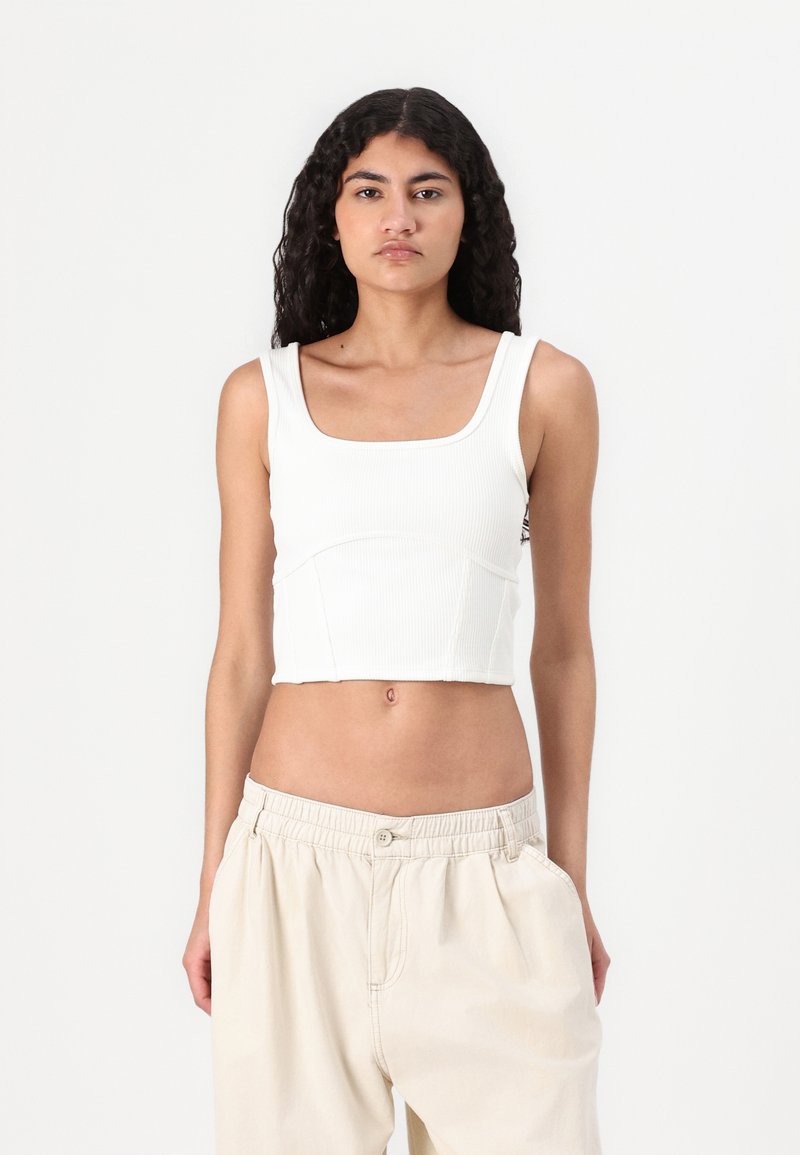 Hvit stripete kuttet tanktopp med firkantet utringning og brede stropper, stylet med beige løstsittende bukser. Ingen synlige logoer eller mønstre.