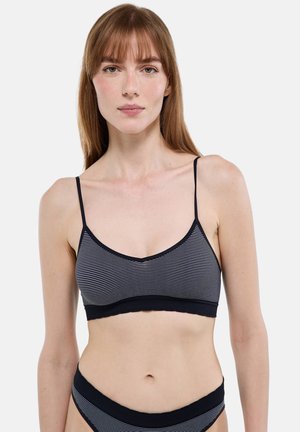 Jeune femme aux cheveux roux raides portant un soutien-gorge rayé noir et blanc et une culotte assortie sur un fond blanc uni.