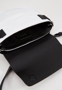 Borsa in pelle nera con una morbida patta di tessuto bianco, dotata di tasca interna e texture liscia. Cinghia regolabile inclusa per versatilità.