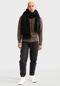 Knit brown sweater, black scarf with fringes, dark jeans, and white sneakers. The outfit features a relaxed fit and textured materials.