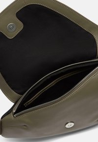 Wnętrze oliwkowozielonej skórzanej torby z czarną podszewką, dwoma zamykanymi na zamek kieszeniami i zapięciem na zatrzask. Gładka tekstura i minimalne przeszycia.