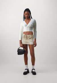Bílý ribrový zkrácený svetr s hlubokým výstřihem do V, béžová mini sukně s páskem, černá strukturovaná kabelka a černé platformové boty.