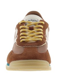 Zapatilla marrón y beige con cordones amarillos, paneles de ante y cuero, y suela de goma, vista desde el frente.