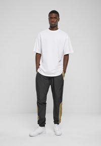 Hvid oversized t-shirt parret med sorte joggers med khaki sidepaneler og hvid piping, færdiggjort med hvide sneakers.