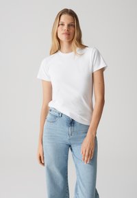 T-shirt bianco in cotone con maniche corte, scollatura rotonda e vestibilità comoda, abbinato a jeans in denim azzurro chiaro a vita alta.